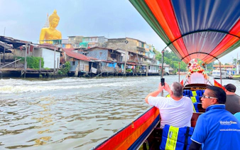 Longtail boat on Bangkok canal passing houses and a large Buddha statue.