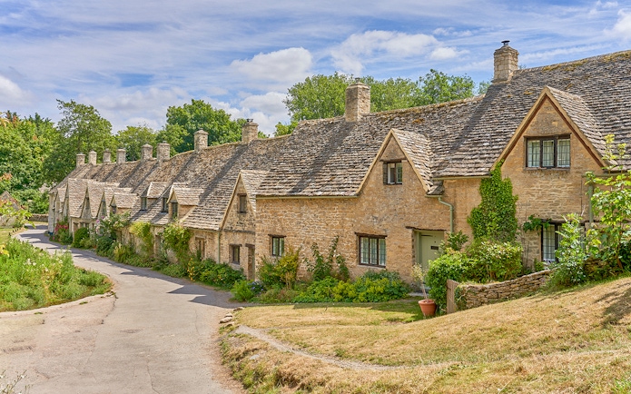 Row of historic stone cottages in Bibury, Cotswolds, surrounded by greenery.