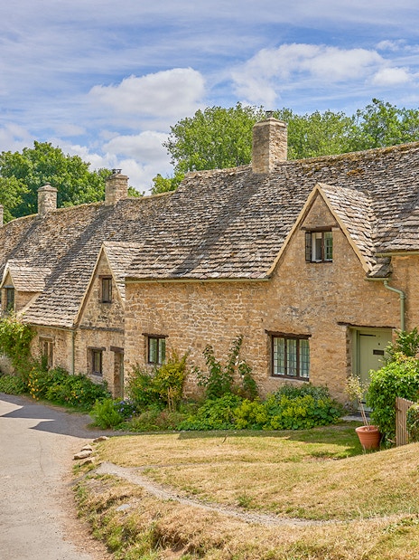 Row of historic stone cottages in Bibury, Cotswolds, surrounded by greenery.