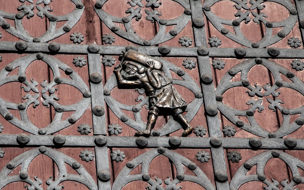 Ornate metalwork on a door in Barcelona's Gothic Quarter, featuring a figure carrying a sack.