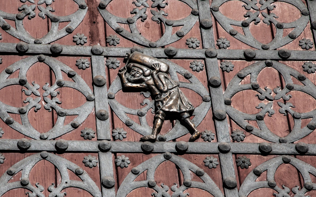 Ornate metalwork on a door in Barcelona's Gothic Quarter, featuring a figure carrying a sack.