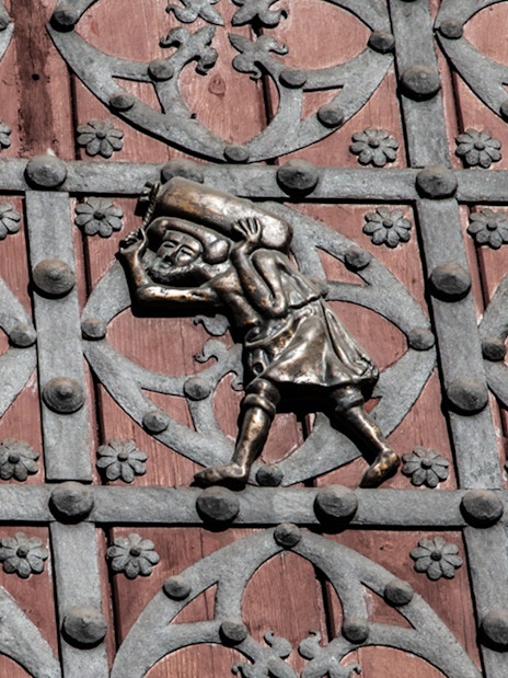 Ornate metalwork on a door in Barcelona's Gothic Quarter, featuring a figure carrying a sack.