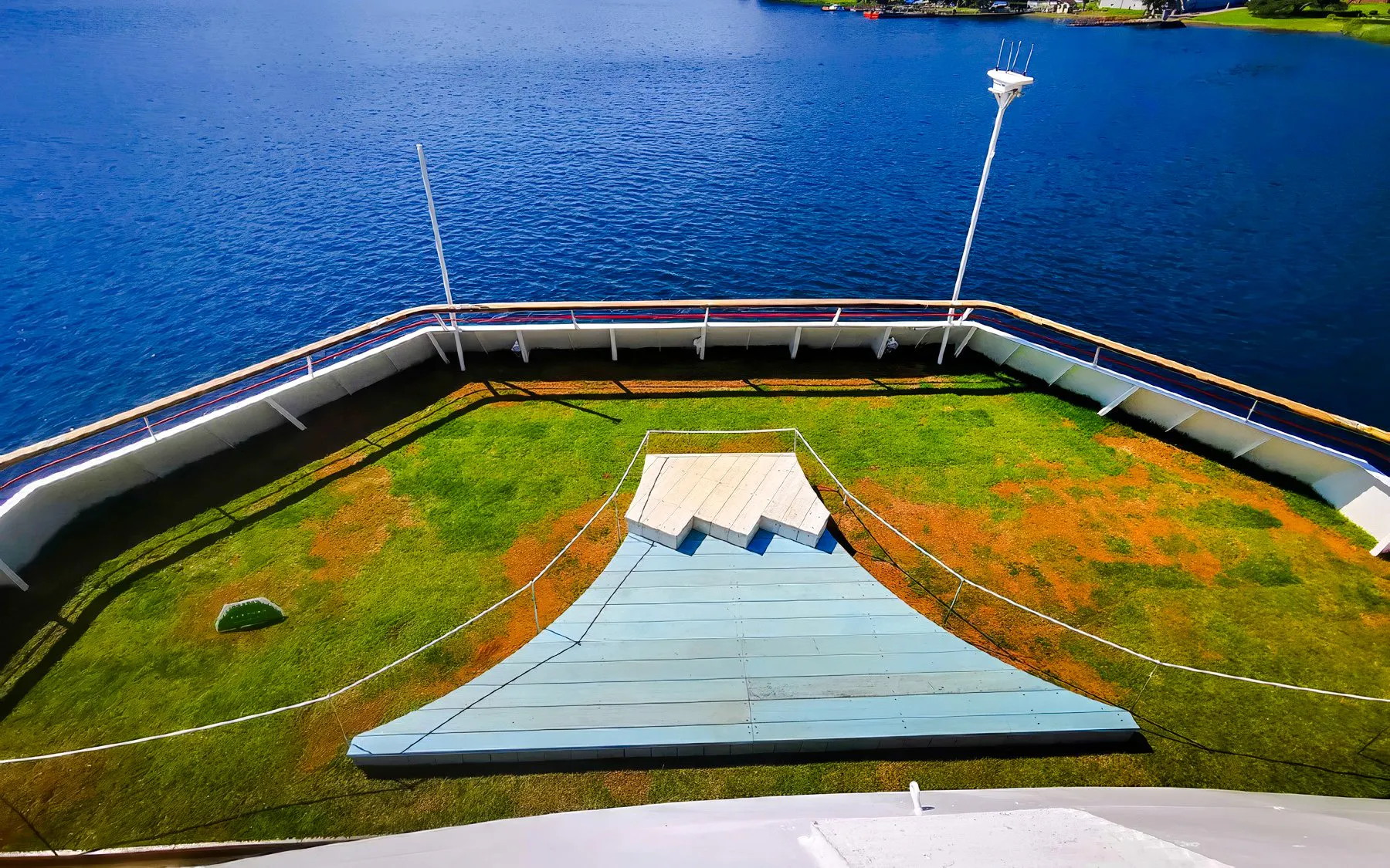 Top deck view from Hakone Sightseeing Cruise overlooking blue water and green lawn.