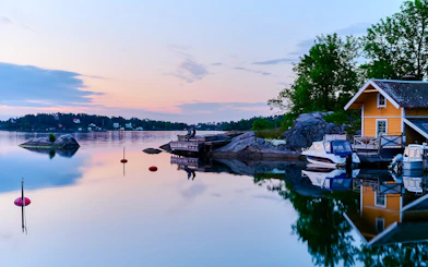 Sunset over Stockholm archipelago with boats and a yellow house by the water.