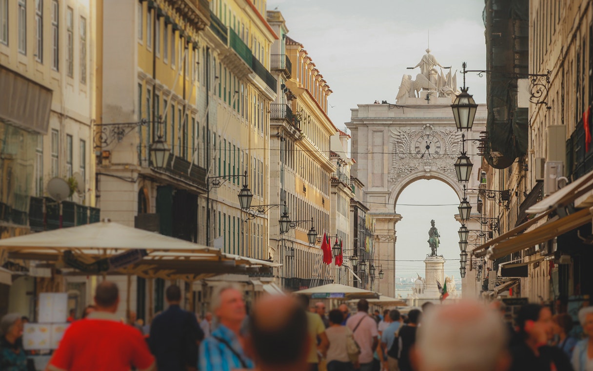 Rua Augusta Arch in Lisbon with bustling street and statue in view.