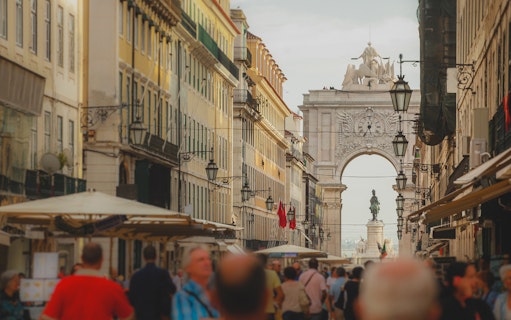 Rua Augusta Arch in Lisbon with bustling street and statue in view.