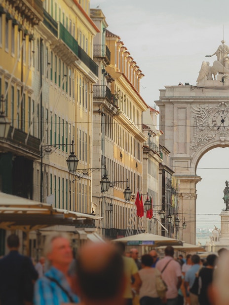 Rua Augusta Arch in Lisbon with bustling street and statue in view.