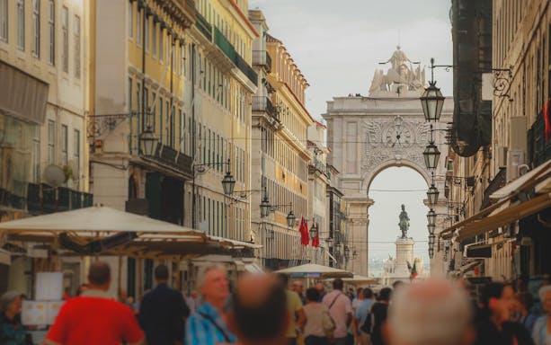 Rua Augusta Arch in Lisbon with bustling street and statue in view.