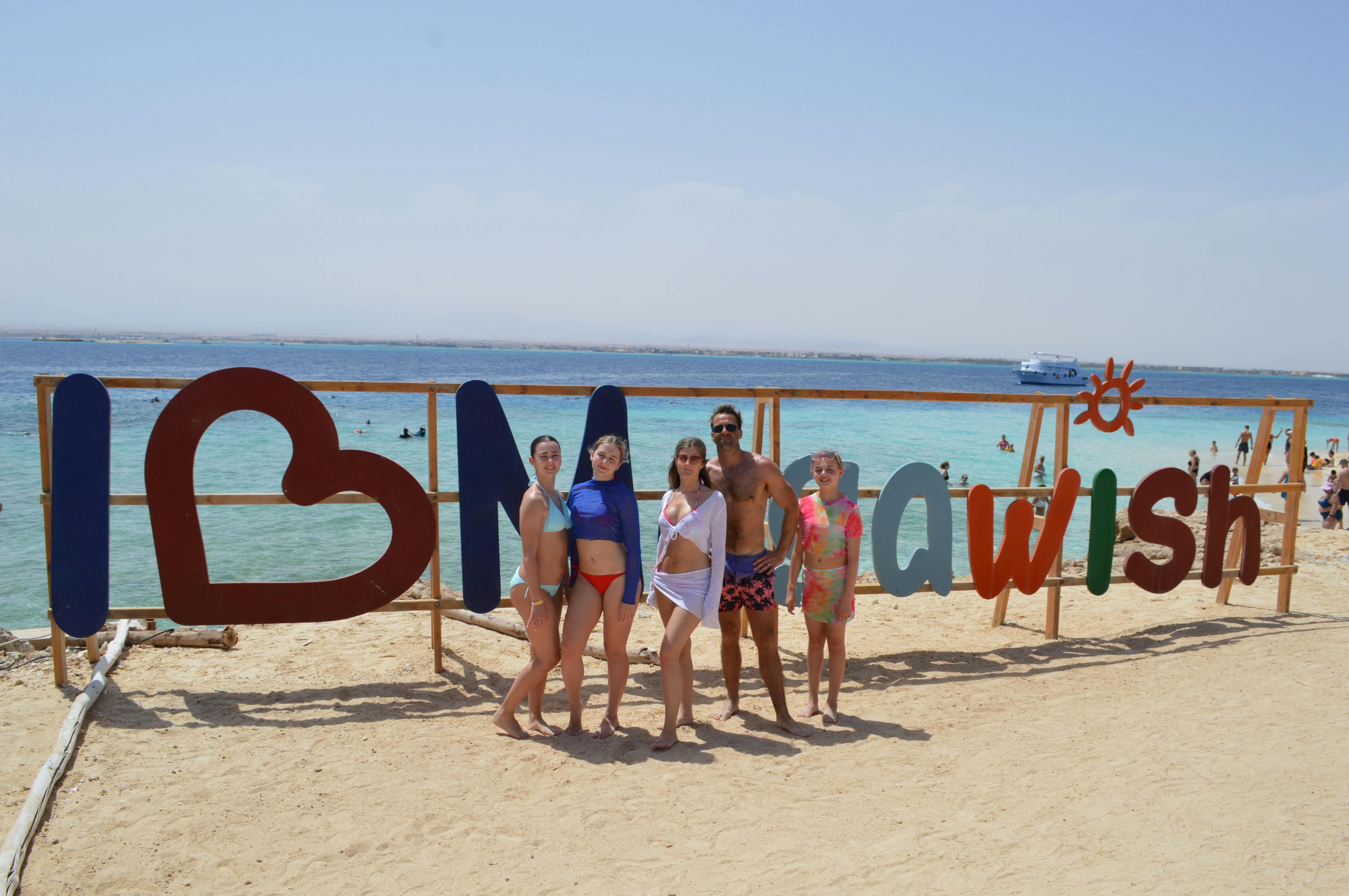 Group posing by "I Love Mahwish" sign on Giftun Island beach, Egypt.