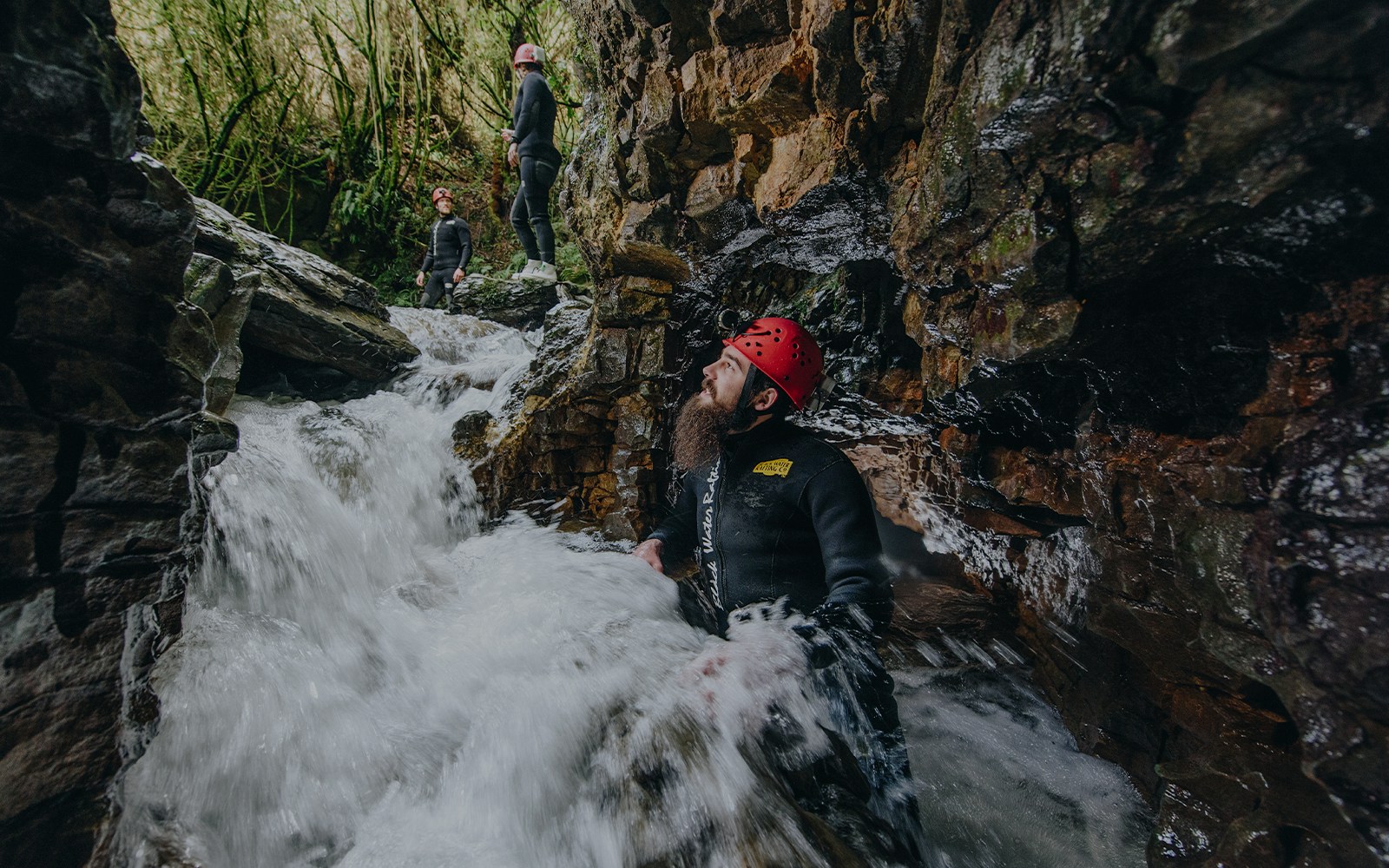 Adventurers in wetsuits and helmets navigate rocky stream in Waitomo cave.