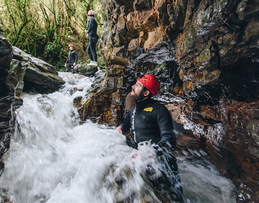 Adventurers in wetsuits and helmets navigate rocky stream in Waitomo cave.