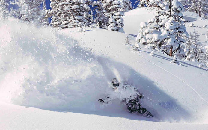 Skier navigating deep powder snow on a mountain slope with Ikon Pass.