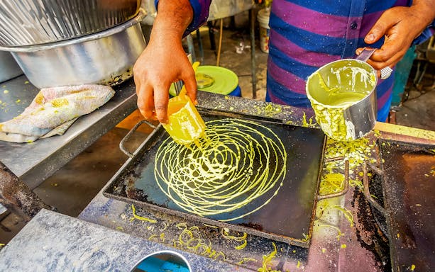 Vendor preparing green batter on a hot griddle, Penang street food.