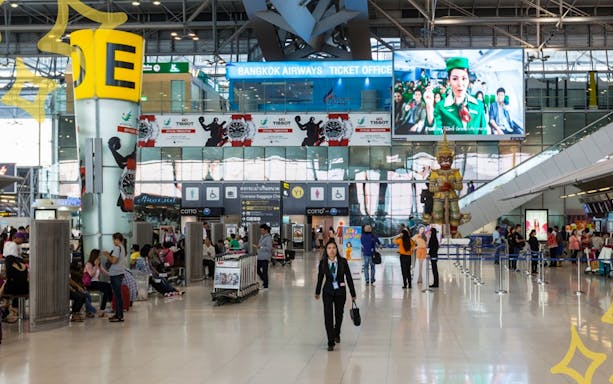Bangkok Suvarnabhumi Airport interior with travelers and ticket office.