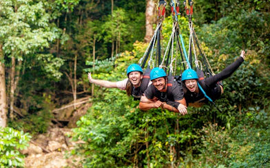 Visitors enjoying a group triple swing at Skypark Cairns amidst lush greenery.