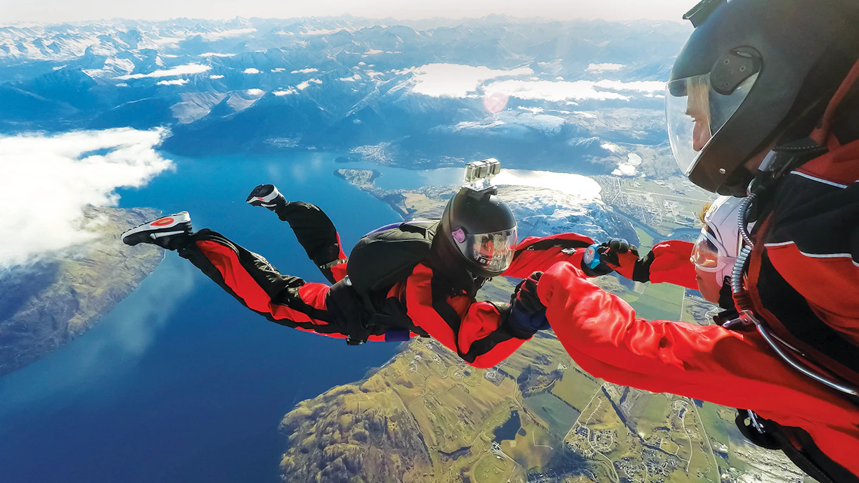 Tandem skydivers over Lake Wakatipu, Queenstown, with mountain views.