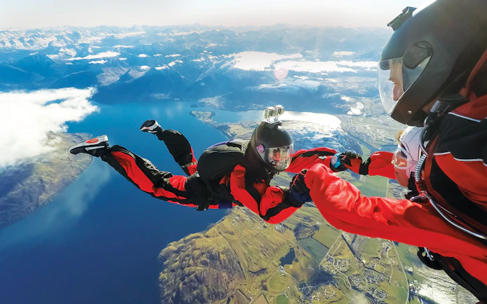 Tandem skydivers over Lake Wakatipu, Queenstown, with mountain views.