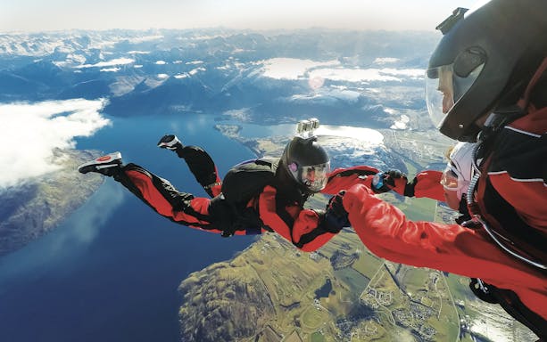 Tandem skydivers over Lake Wakatipu, Queenstown, with mountain views.