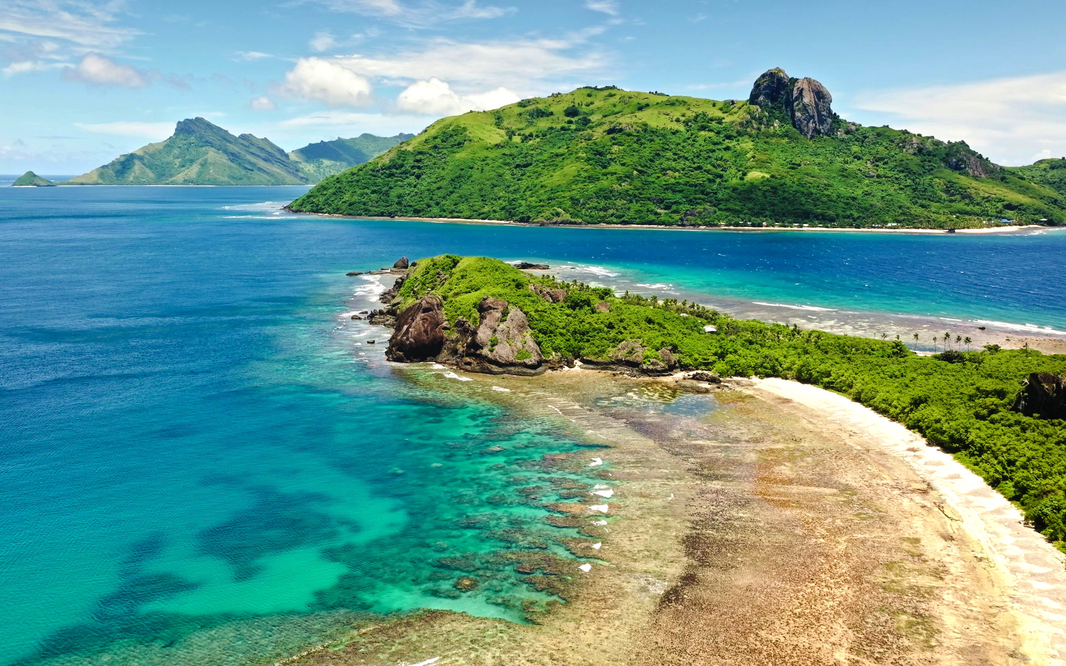 Aerial view of Kuata Island, Fiji, showcasing turquoise lagoon, coral reefs, sandy beach, and lush greenery.
