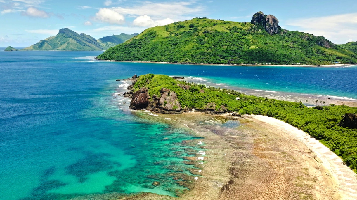Aerial view of Kuata Island, Fiji, showcasing turquoise lagoon, coral reefs, sandy beach, and lush greenery.