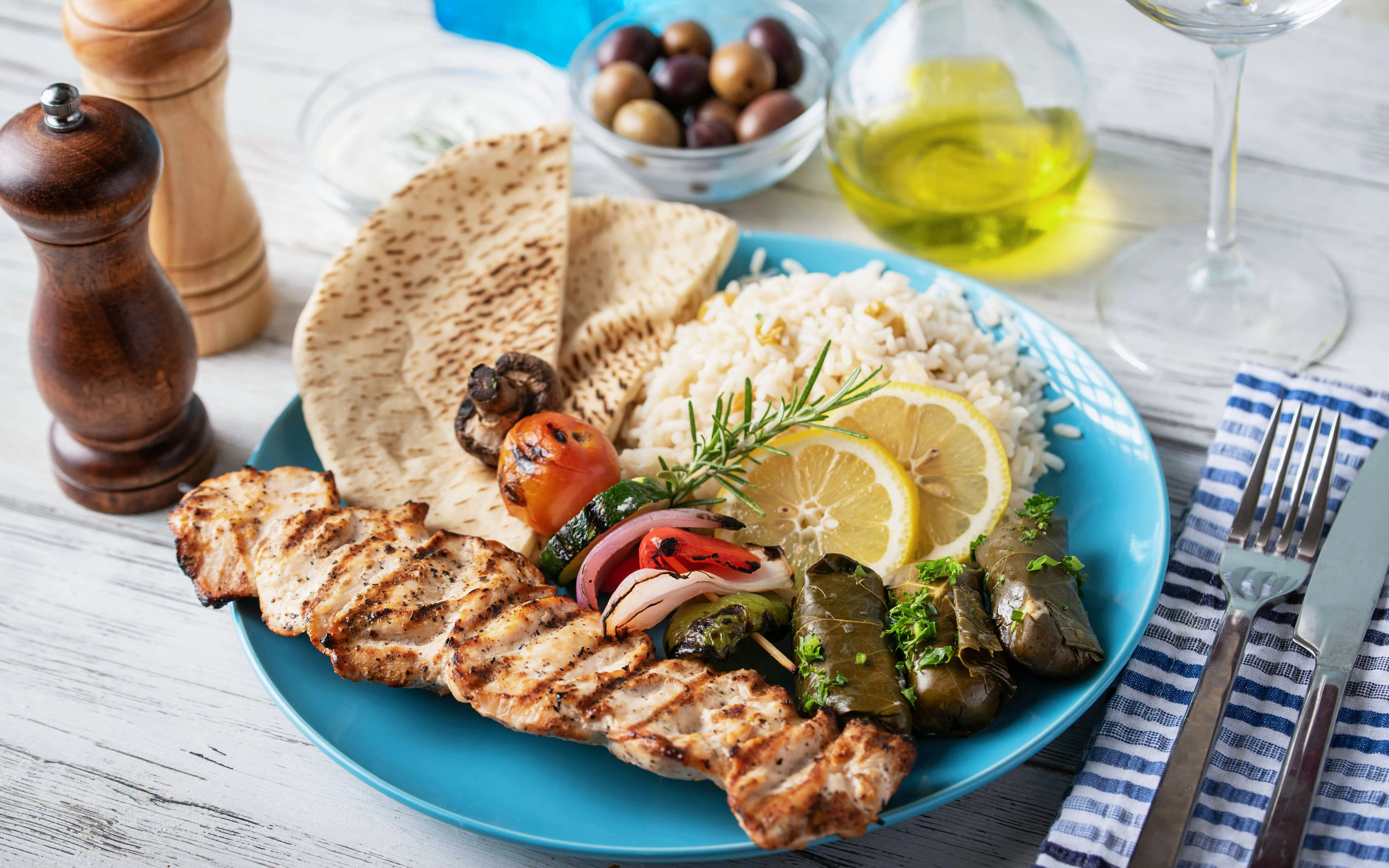 Assorted Greek food platter with souvlaki, rice, pita, and dolmades on a blue plate.
