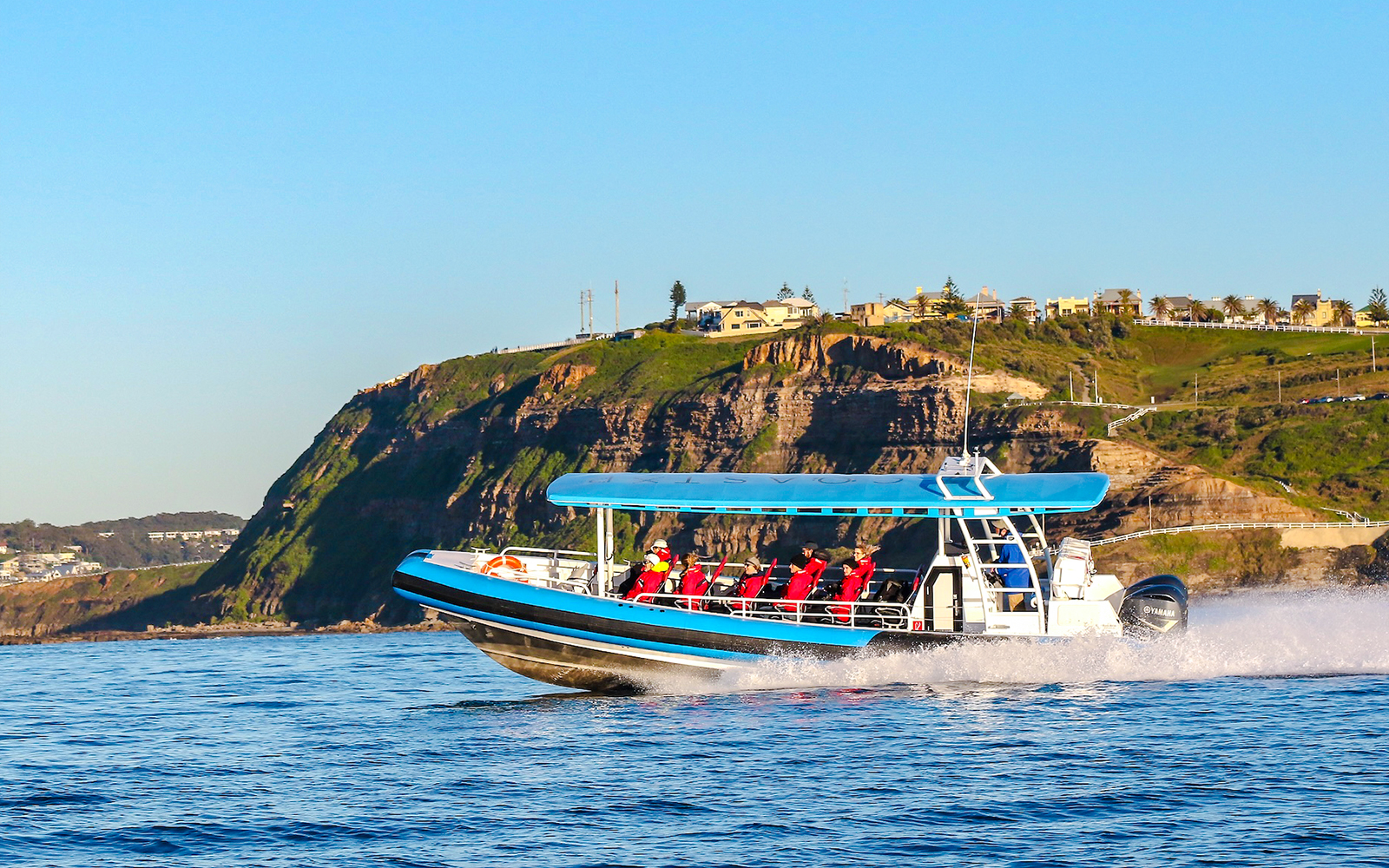 Whale watching boat with people near cliffs in Newcastle, Australia.