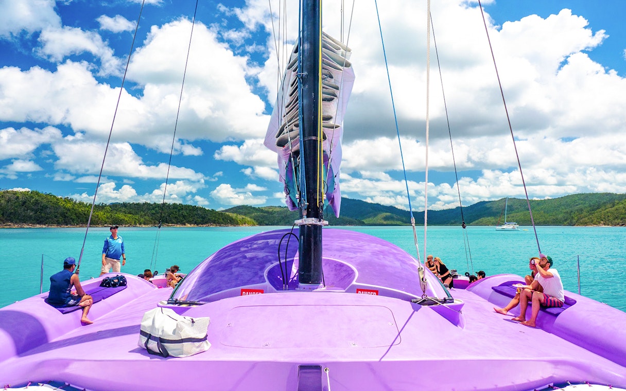Sailing on a purple catamaran in Airlie Beach with passengers enjoying the view.