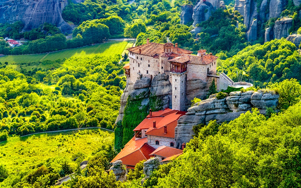 Meteora monastery perched on rock formation surrounded by lush greenery, Greece.