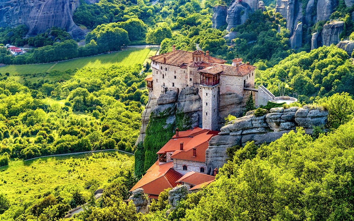 Meteora monastery perched on rock formation surrounded by lush greenery, Greece.