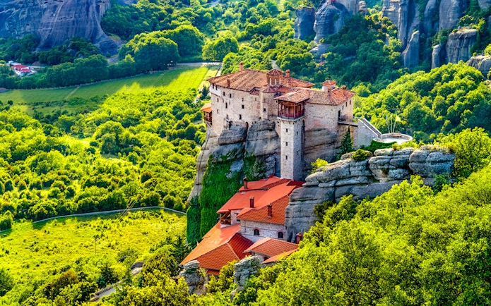 Meteora monastery perched on rock formation surrounded by lush greenery, Greece.