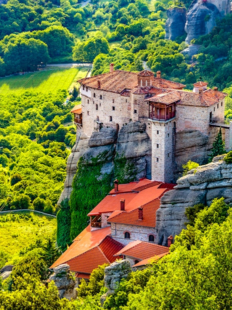 Meteora monastery perched on rock formation surrounded by lush greenery, Greece.