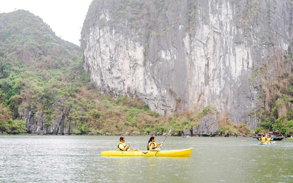 Kayakers paddling near limestone cliffs in Ha Long Bay, Vietnam.