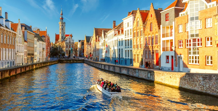 Tourist boat on Spiegelrei canal near Jan Van Eyck Square, Bruges, Belgium in morning light.