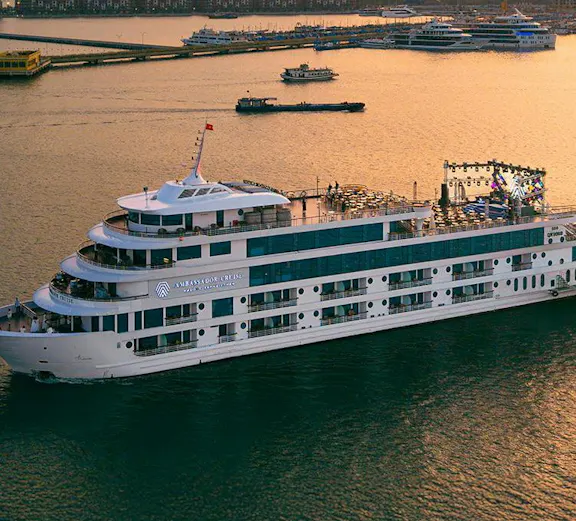 Aerial view of Ambassador cruise ship sailing near city harbor at sunset.