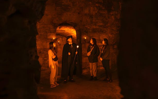 Guide narrating ghost stories to a group during an underground ghost tour in Edinburgh