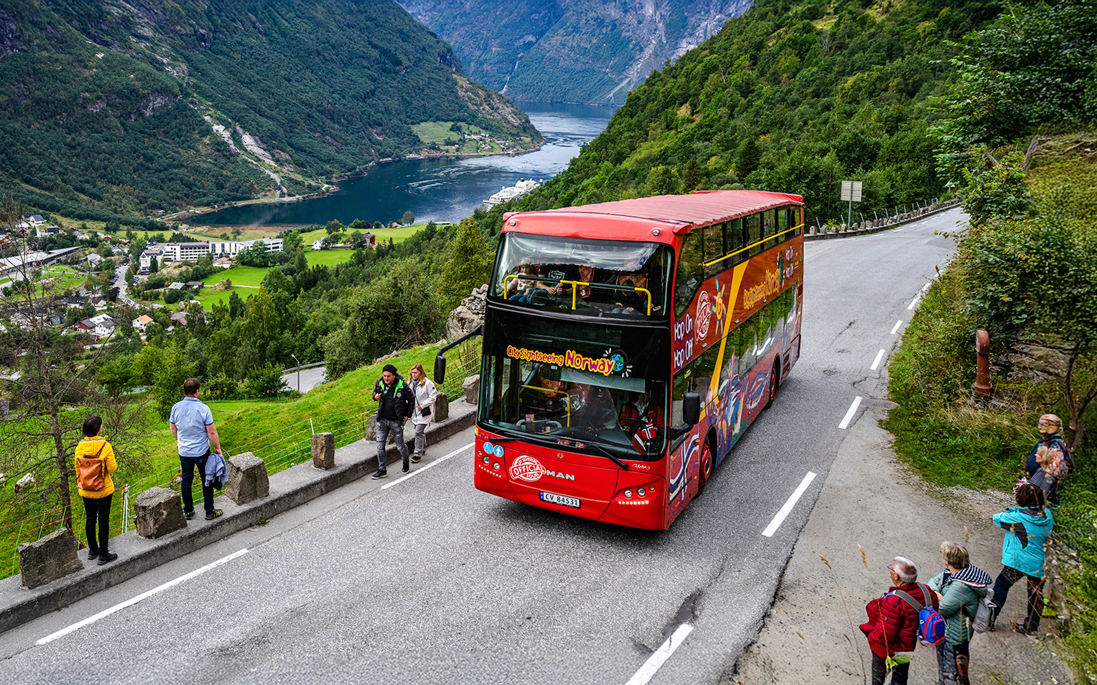 Red double-decker bus on Geiranger Hop-on Hop-off tour, Norway, with fjord view.