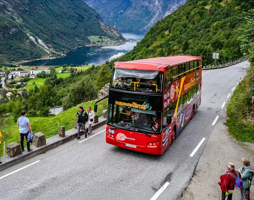 Red double-decker bus on Geiranger Hop-on Hop-off tour, Norway, with fjord view.
