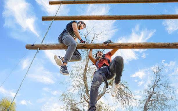 Man climbing Jacob's Ladder with trainer at Aventura Parks.