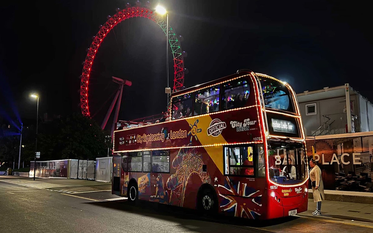 Open-top bus with Christmas lights near the illuminated London Eye at night.