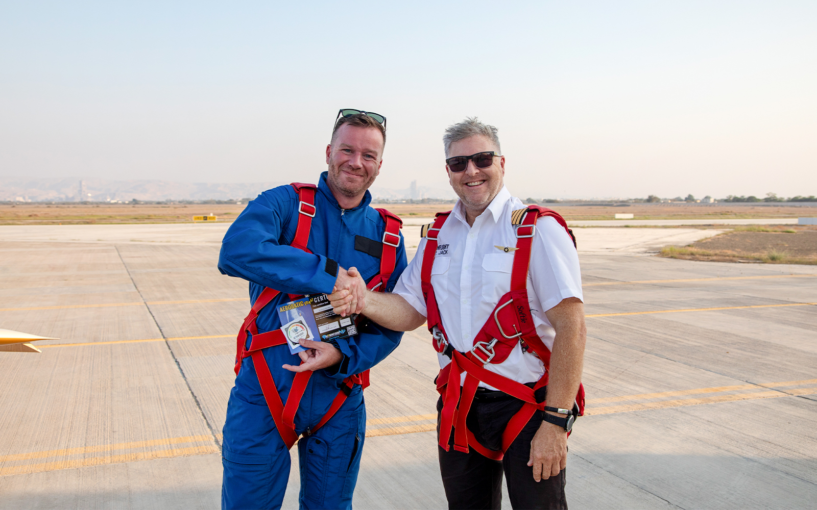 Pilot presenting post-flight certificate to passenger on airfield.