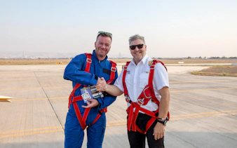 Pilot presenting post-flight certificate to passenger on airfield.