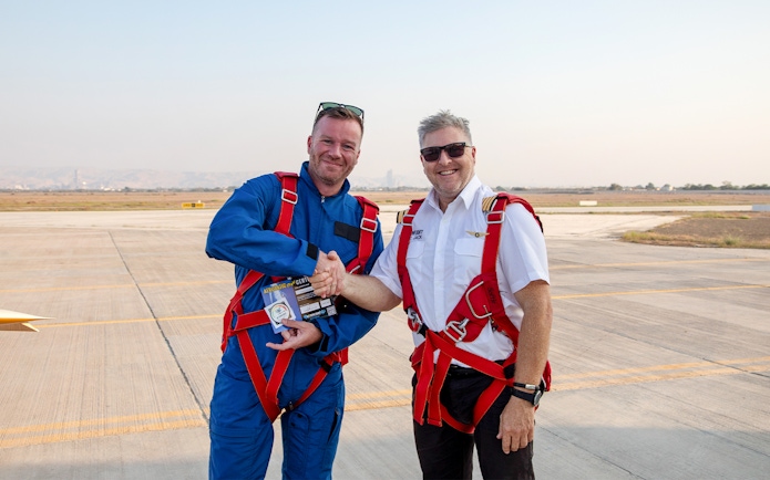 Pilot presenting post-flight certificate to passenger on airfield.