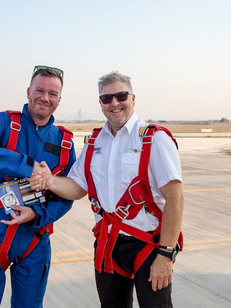 Pilot presenting post-flight certificate to passenger on airfield.