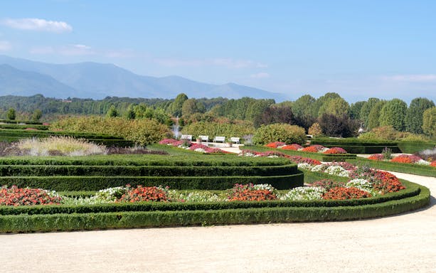 Palace of Venaria gardens with colorful flower beds and distant mountains.