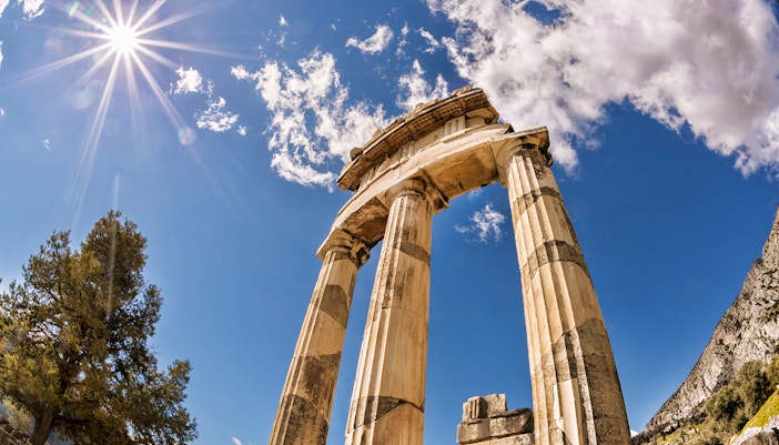 Ancient columns of the Tholos at Delphi, Greece, under a bright sky.