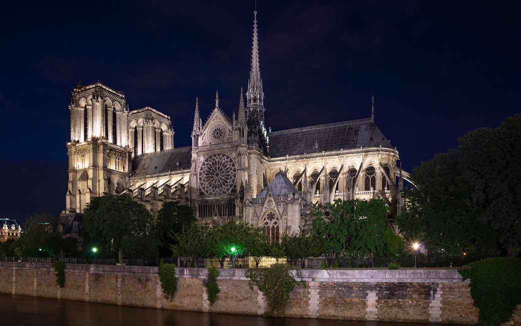 Notre Dame Cathedral illuminated at night in Paris, viewed from across the Seine River.