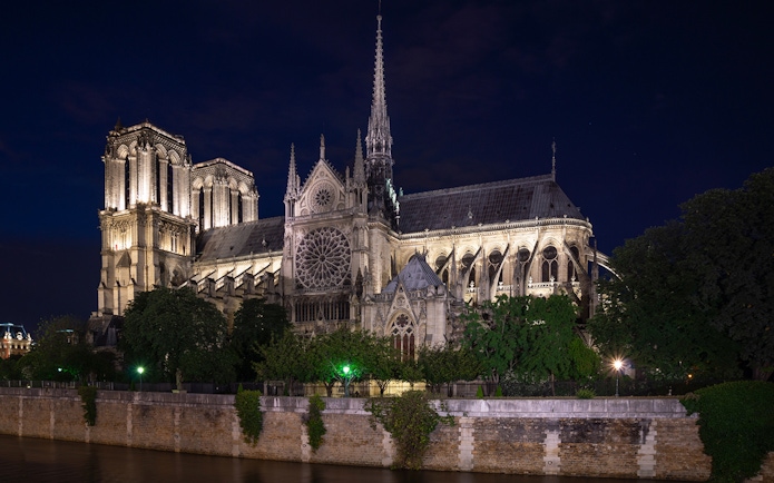 Notre Dame Cathedral illuminated at night in Paris, viewed from across the Seine River.