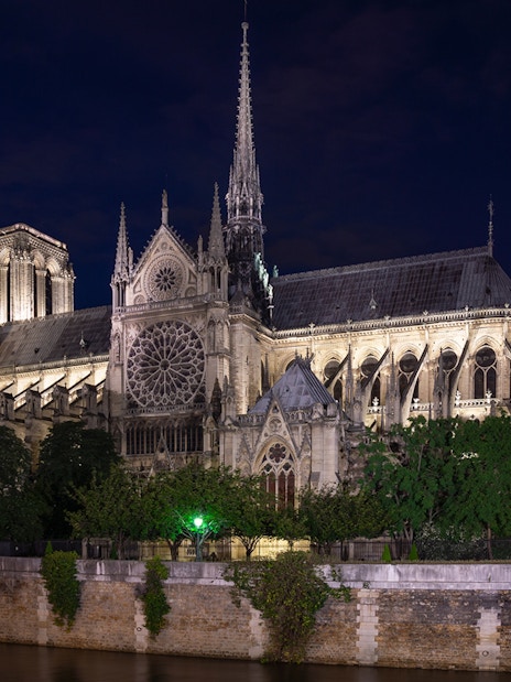 Notre Dame Cathedral illuminated at night in Paris, viewed from across the Seine River.