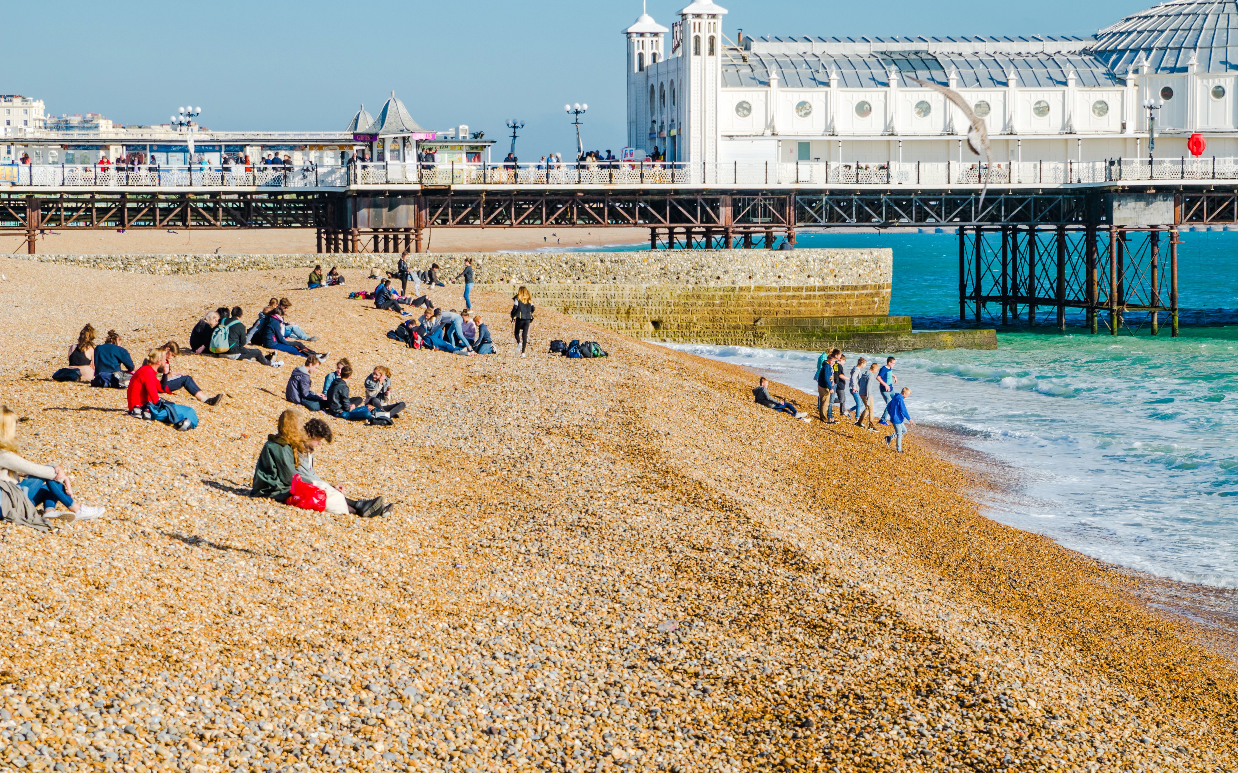 People relaxing on Brighton Beach, Phillip Island, with a pier and ocean in the background.
