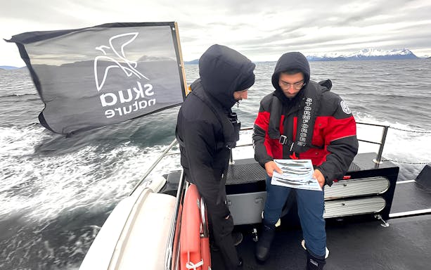 Guests discussing whale-watching guide on a heated boat trip in Norway.